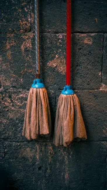 Gros plan de personnes nettoyant un sol en bois avec un balai et une pelle à poussière à l’intérieur.