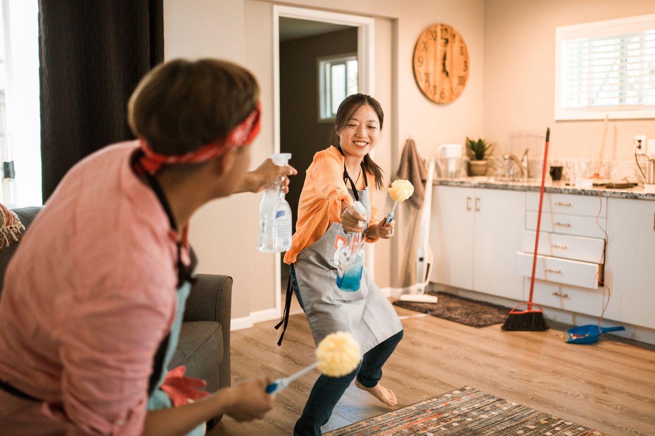 Asian couple enjoying themselves while tidying their home, creating a cheerful atmosphere.